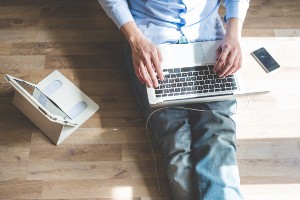 Man sitting on floor working on laptop, sitting by smartphone and tablet