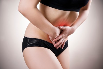 A woman in black undergarments grabs her lower abdomen in pain, with a red glow over her abdomen - vaginal mesh injury