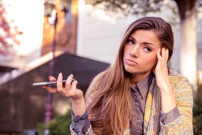 An annoyed woman holds her cellphone out like she's not listening to the caller - nuisance calls