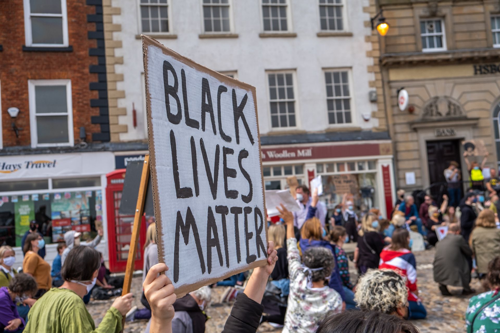 Richmond, North Yorkshire, UK - June 14, 2020: A Black Lives Matter placard is held up above a kneeling crowd at a protest in Richmond, North Yorkshire โ BLM UK