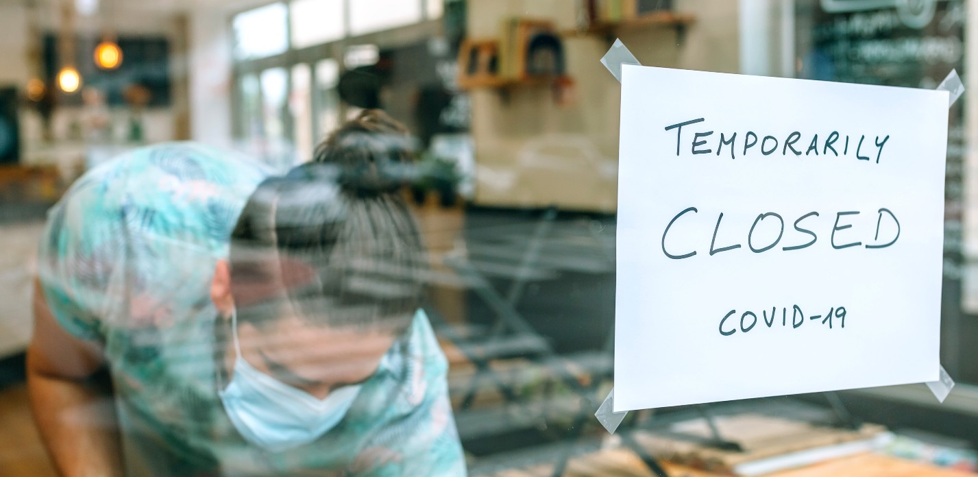 Man cleans up inside restaurant with a sign in the window that reads "temporarily closed covid-19" - lockdown legal challenge