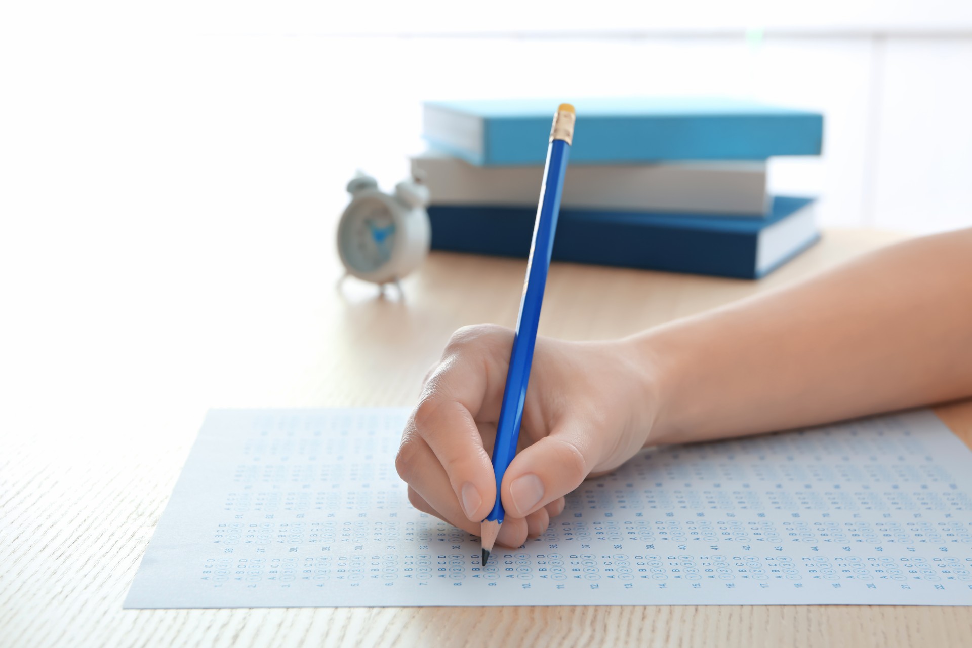 A person's hand holds a pencil while filling in circles on an exam sheet - Scotland exam grades