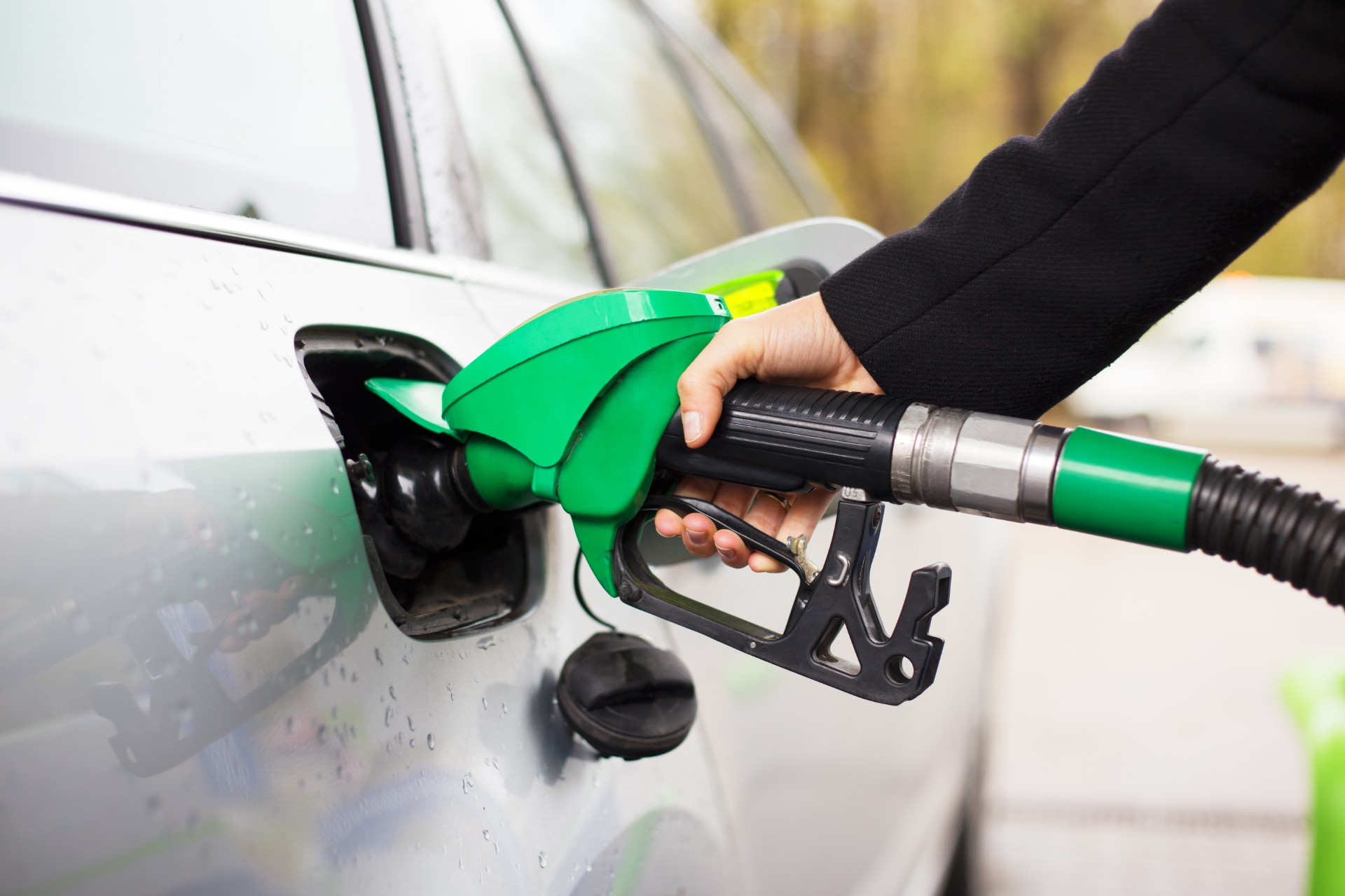 Closeup of person putting fuel in their vehicle on a rainy day - petrol prices