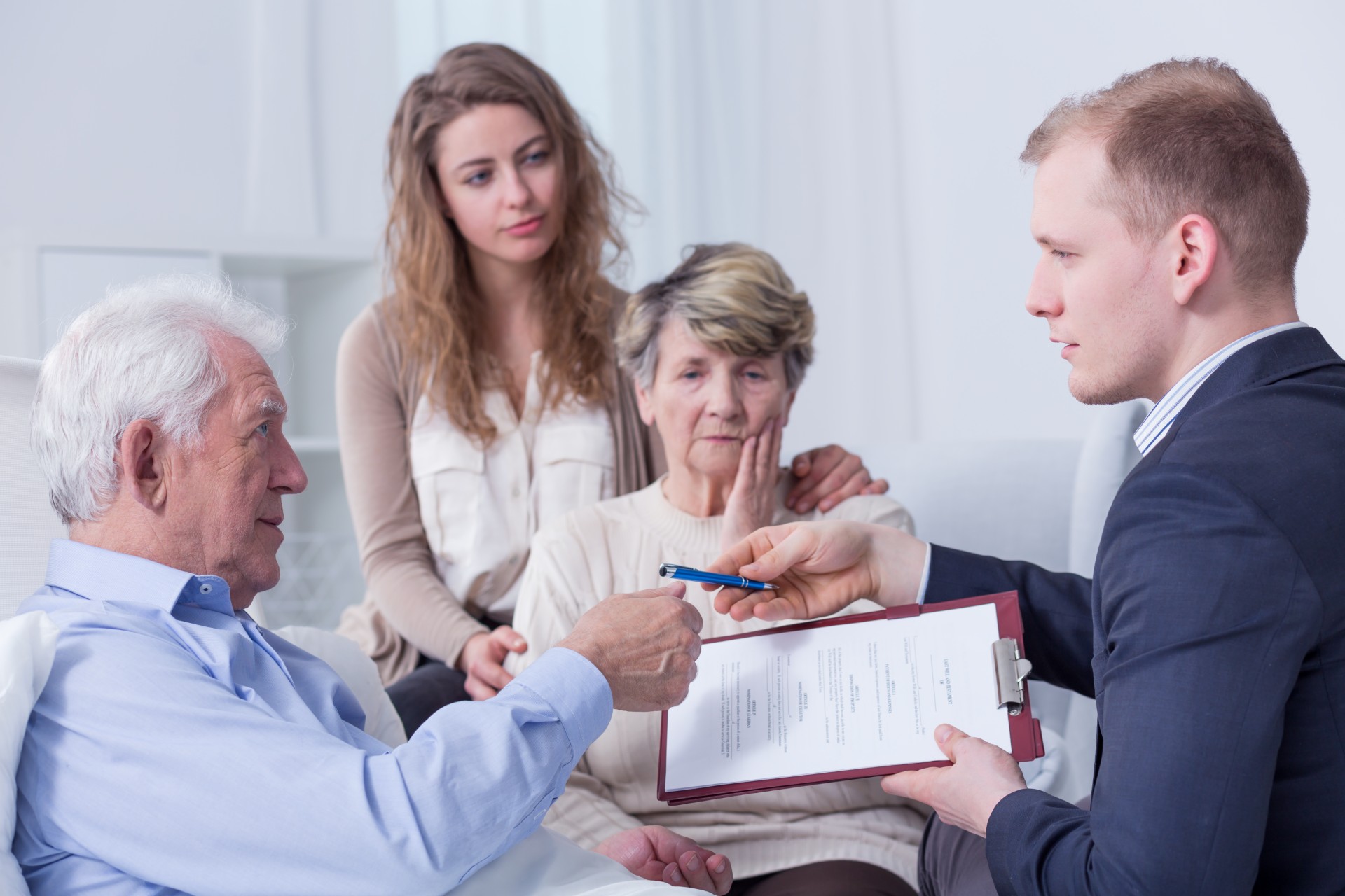 Older man signs paperwork for man in suit as family watches - assisted dying