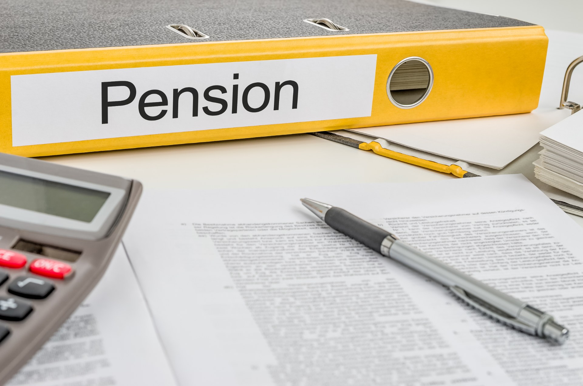 A yellow binder labeled "Pension" on the spine lies with a calculator, pen and other paperwork - pension age