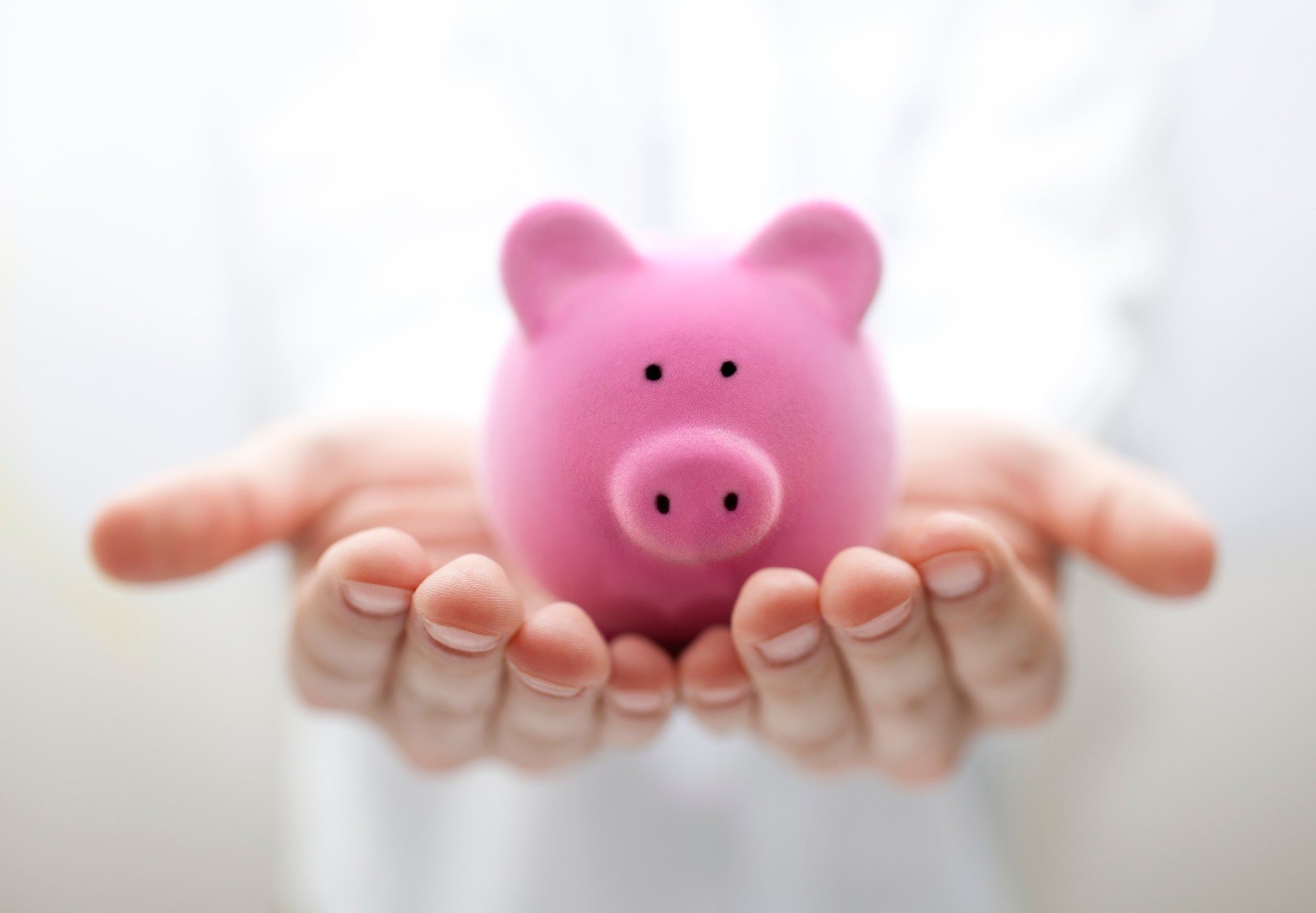 Hands with soft focus hold pink piggy bank forward - child trust fund