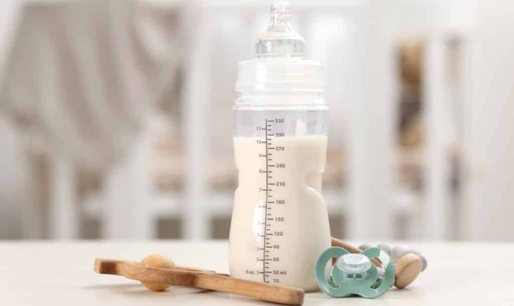 Feeding bottle with baby formula, pacifier and toys on white table indoors