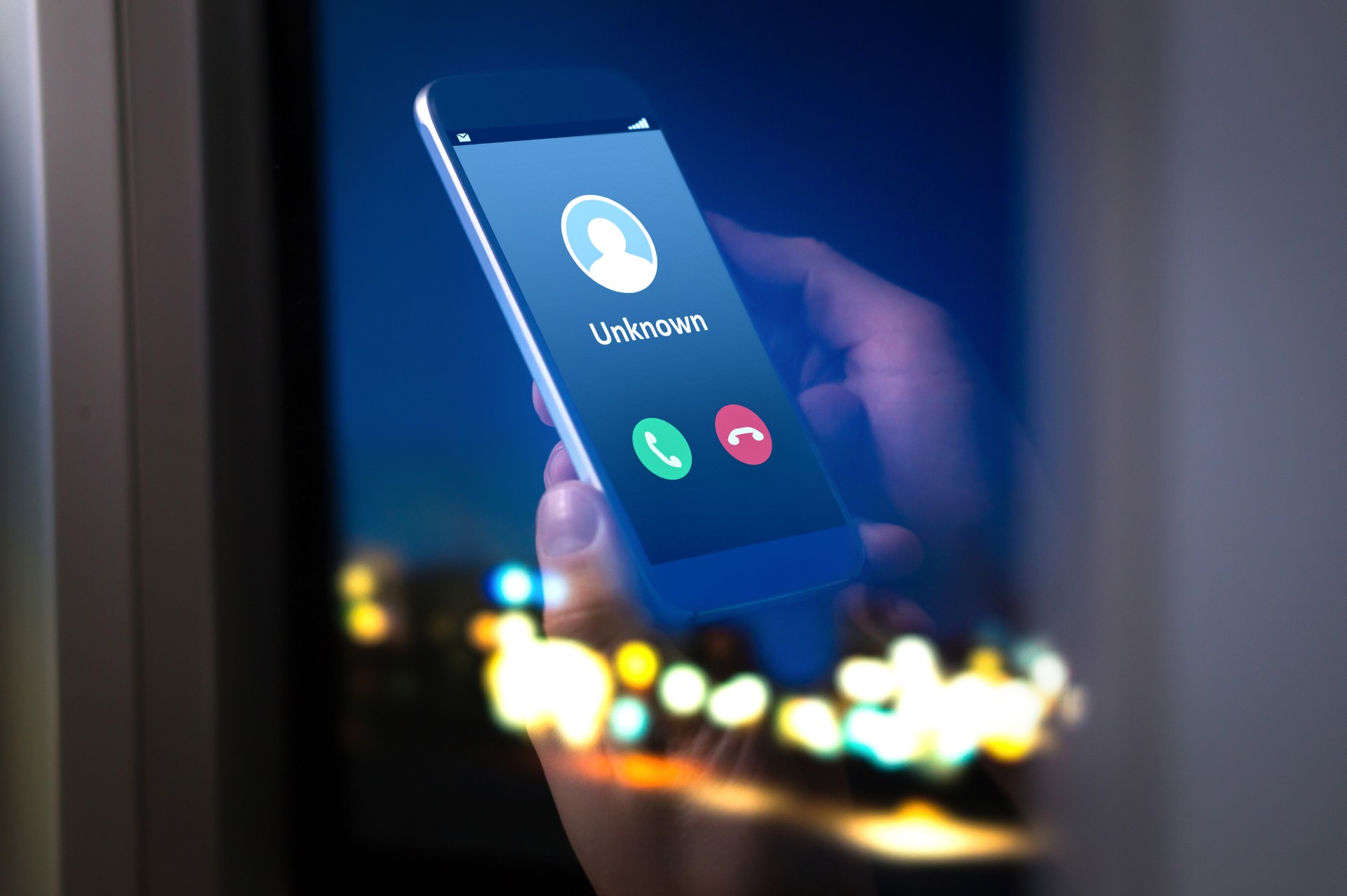 Window reflection showing hands holding a smartphone receiving a call from an unknown caller