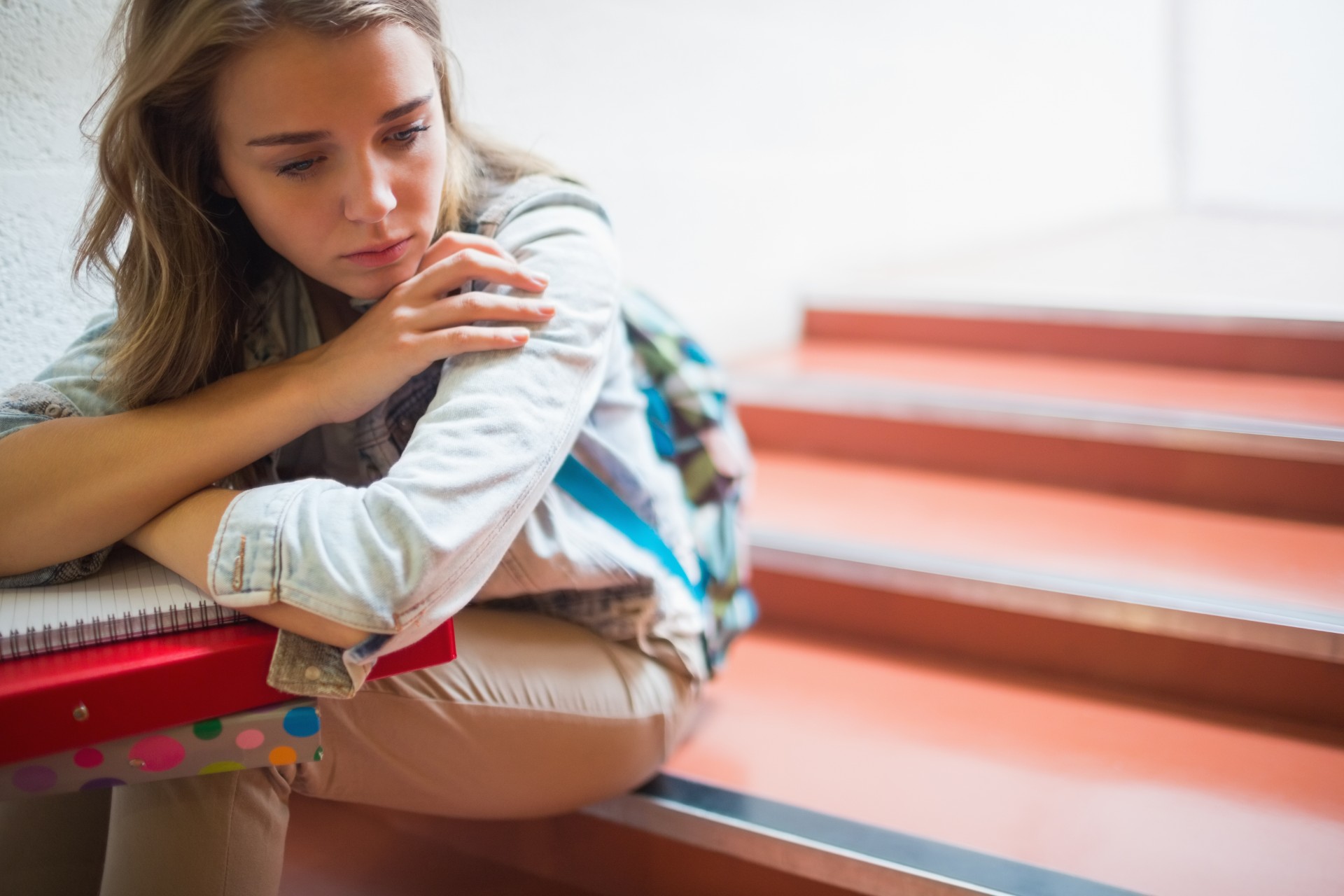 Upset teen girl sits in school stairwell with notebook and binder - A-level exam grades