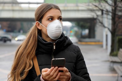 Woman outdoors, wearing mask and holding smartphone - UK test and trace